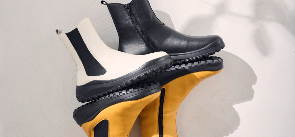 Three pairs of ankle boots stacked: one black, one white, and one yellow, showcasing a stylish design against a light background.
