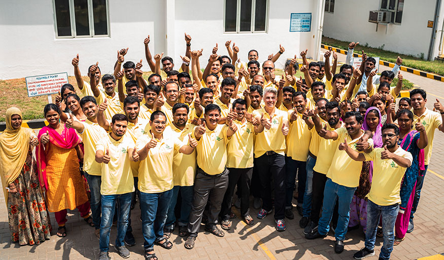 Large group of people in yellow shirts with thumbs up, gathered outside a building