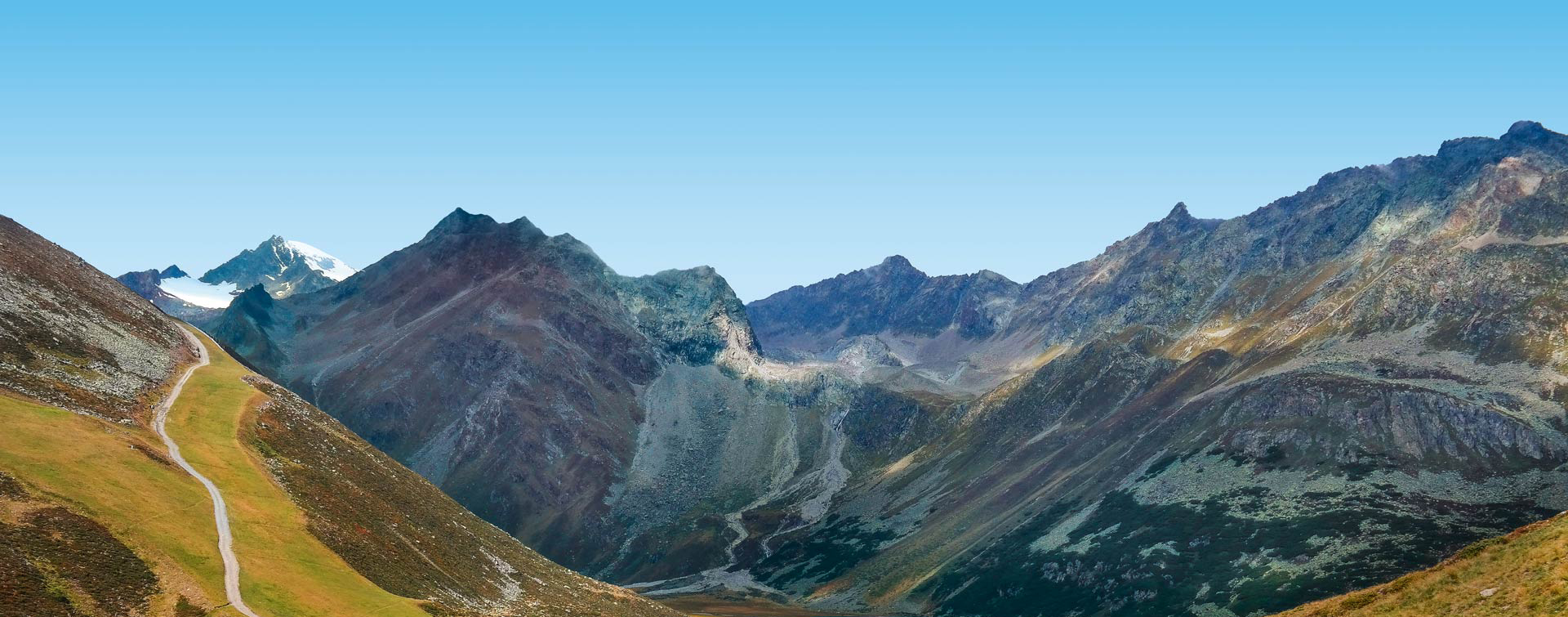 A scenic landscape of a mountain range with a winding path and a clear blue sky