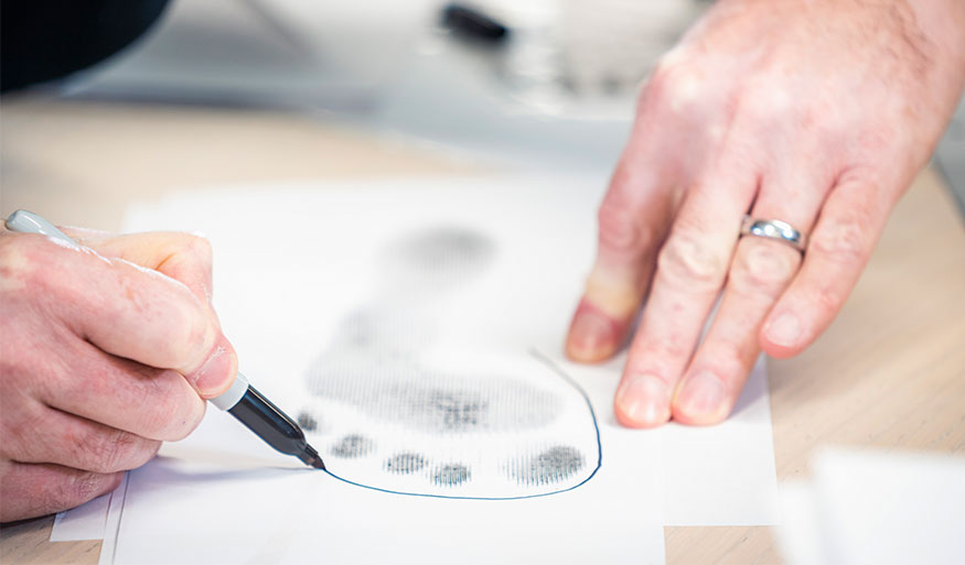 Close-up of a person drawing a footprint on paper with a black marker