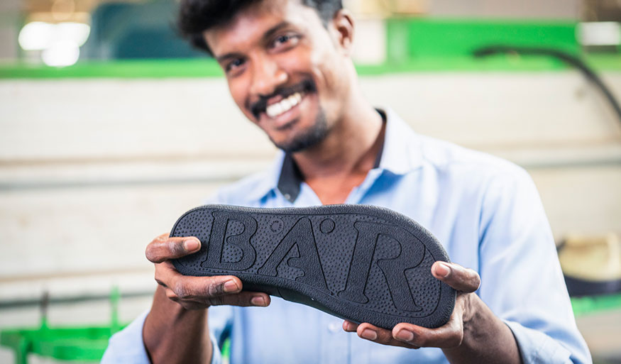 Man in a blue shirt holding a BÄR shoe sole with a smile