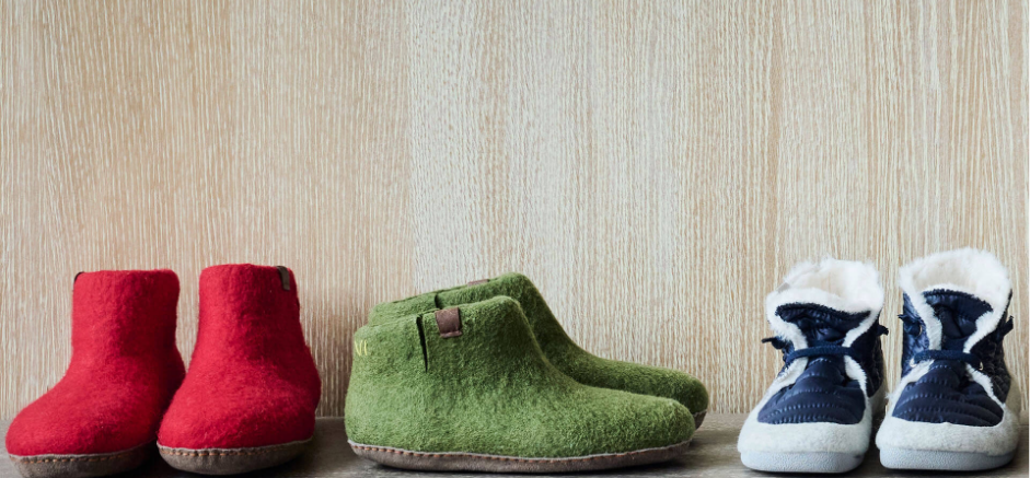 Red and green wool slippers alongside blue winter boots on a wooden floor