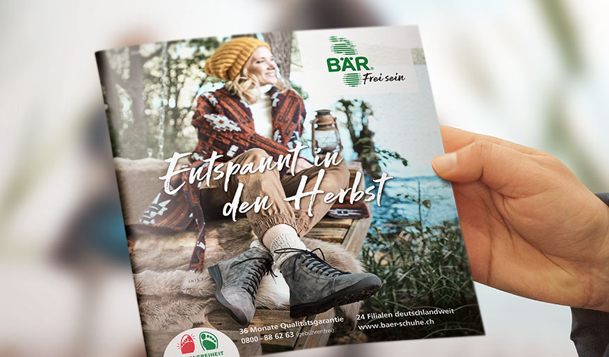 Person holding BÄR footwear catalog featuring fall fashion theme with a woman sitting outdoors in warm clothing and boots.