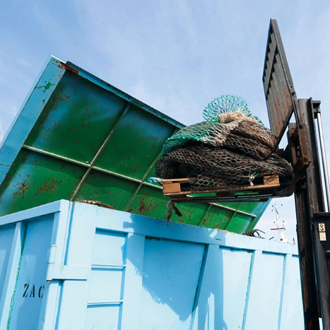 A forklift lifts a pallet covered with nets into a large blue container under a clear sky.