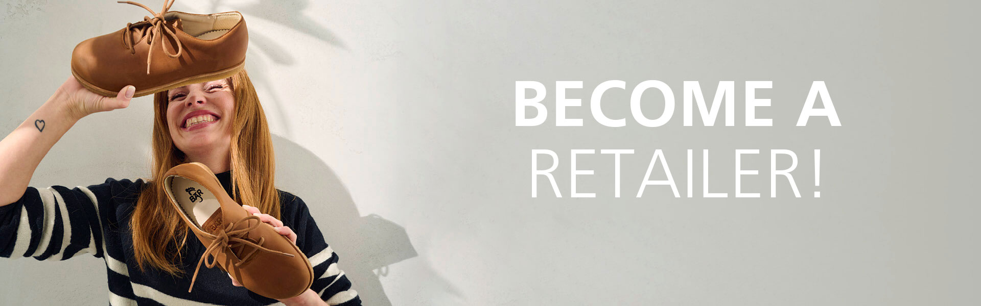 Smiling woman holds brown shoes, encouraging retailers to join the brand