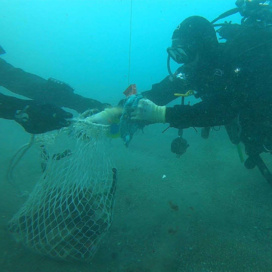 Underwater scene of two divers removing debris from the ocean floor with a net.