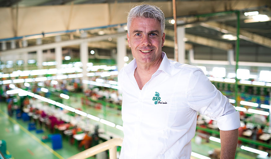 Smiling man in white shirt with logo, standing in a vibrant factory environment