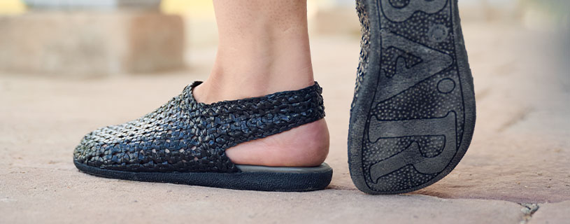 Person wearing black woven slip-on shoes, showing both the top and sole