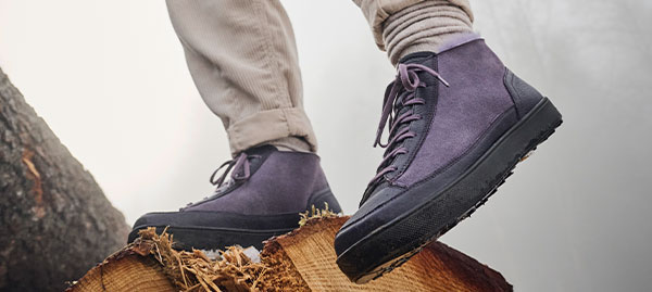 A person wearing purple hiking boots standing on a cut tree stump, showcasing outdoor footwear