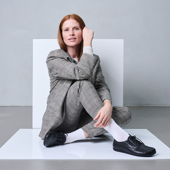 Woman sitting on the floor wearing a checkered suit and black shoes