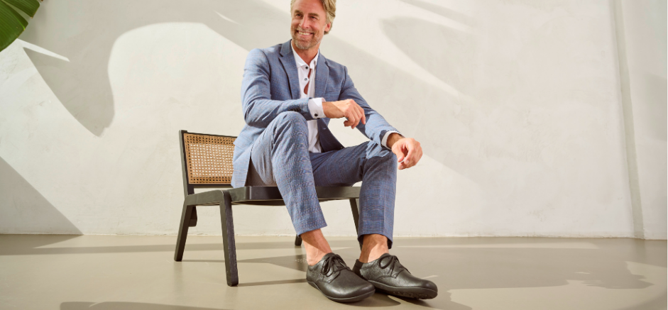 Man wearing a blue suit and black shoes, sitting on a modern chair against a white background