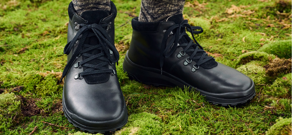 Close-up of durable black hiking boots with laces, standing on a green, moss-covered forest ground.