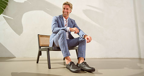 Man in blue suit and leather shoes sitting on a chair, casting shadow on white wall