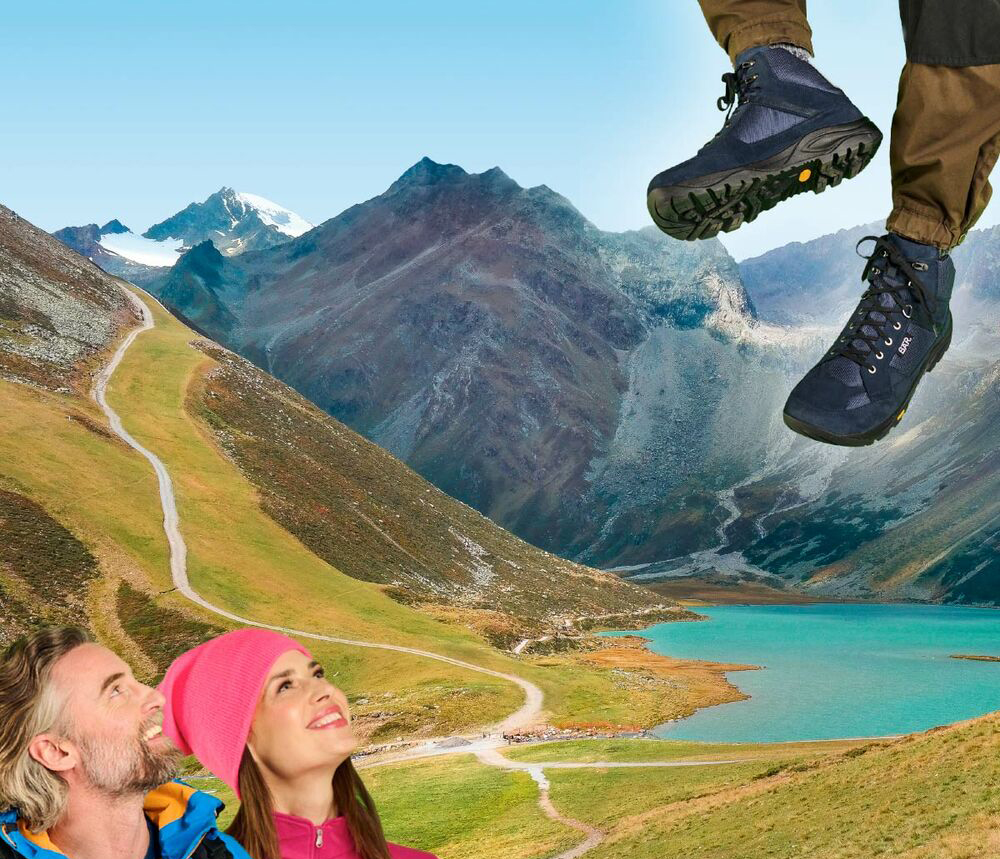 Couple looking at mountains while standing on a trail, wearing hiking boots in alpine scenery.