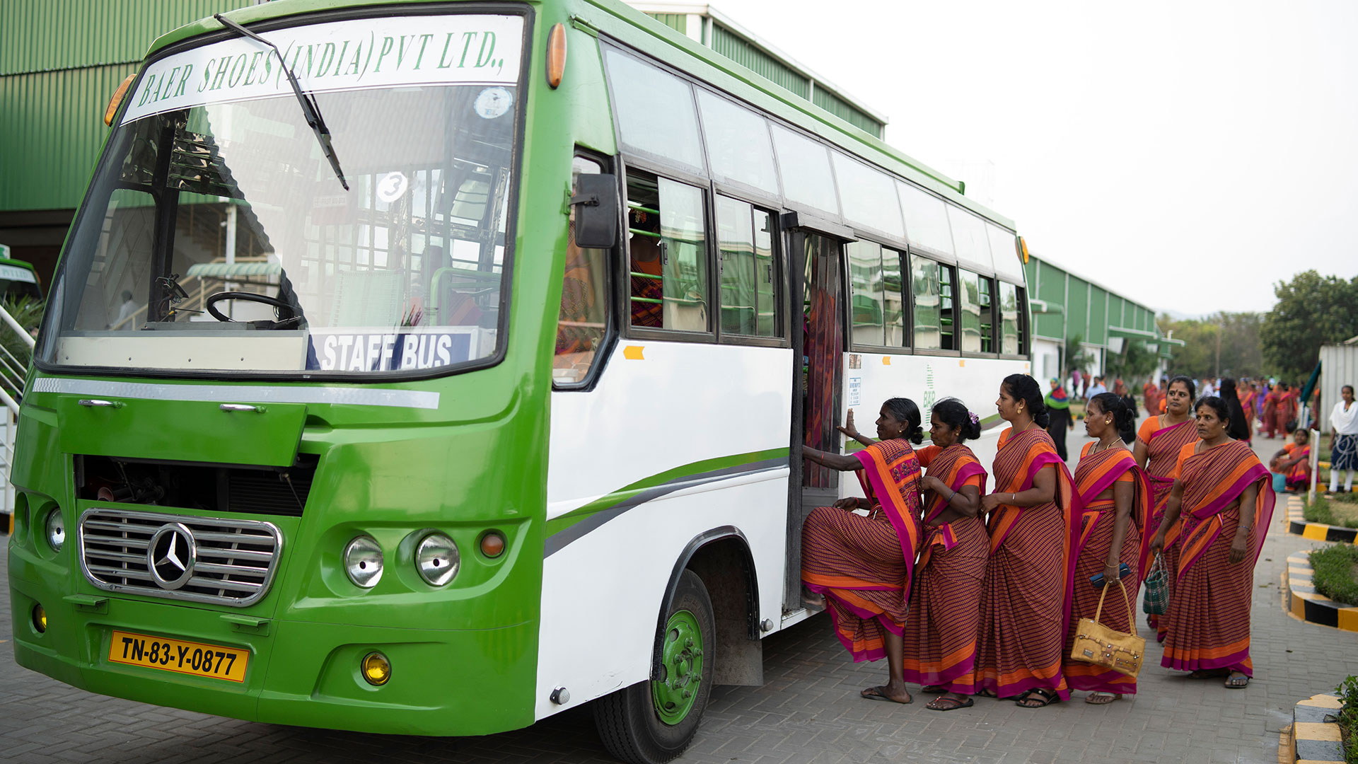 A group of women in traditional sarees getting on a green and white staff bus
