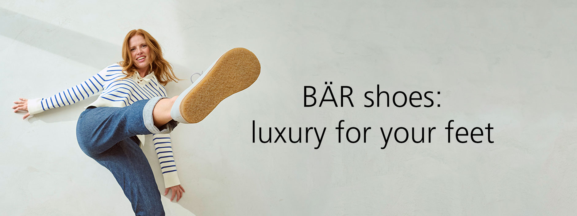 Woman in casual outfit showing the sole of a BÄR shoe with text 'BÄR shoes: luxury for your feet'