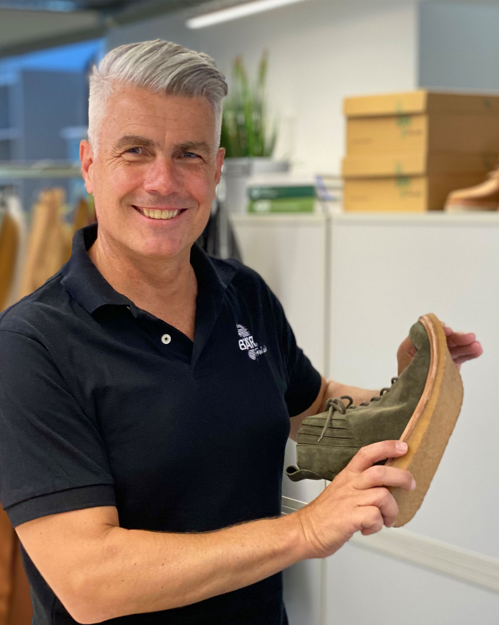 Smiling man showing a green shoe with a cork sole in a shop environment