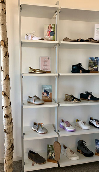 A white shelving unit displaying a selection of men's and women's shoes, including athletic and casual styles, with a birch tree in the foreground.