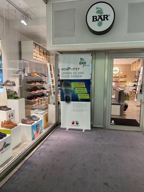 Entrance of a BÄR shoe store featuring a shoe display and a sign promoting their foot scanning service inside.