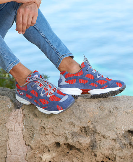 Person wearing blue and red sneakers sitting on a rock by the sea